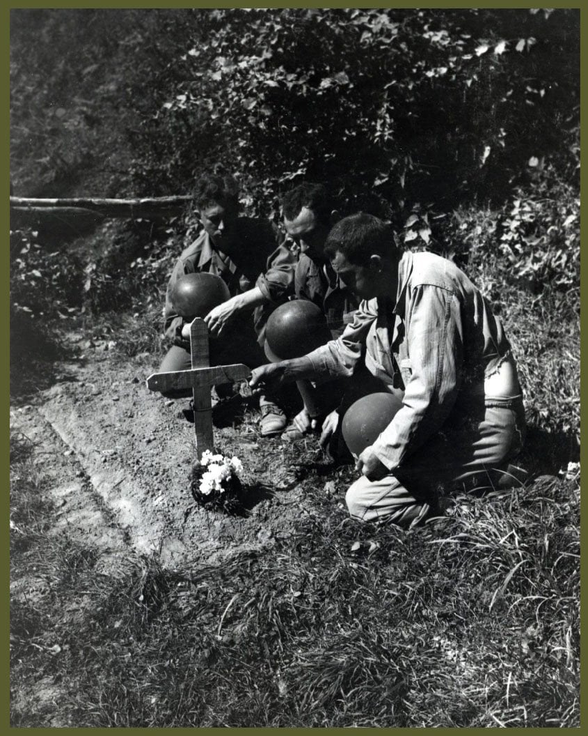 Soldiers kneeling beside a grave in Normandy