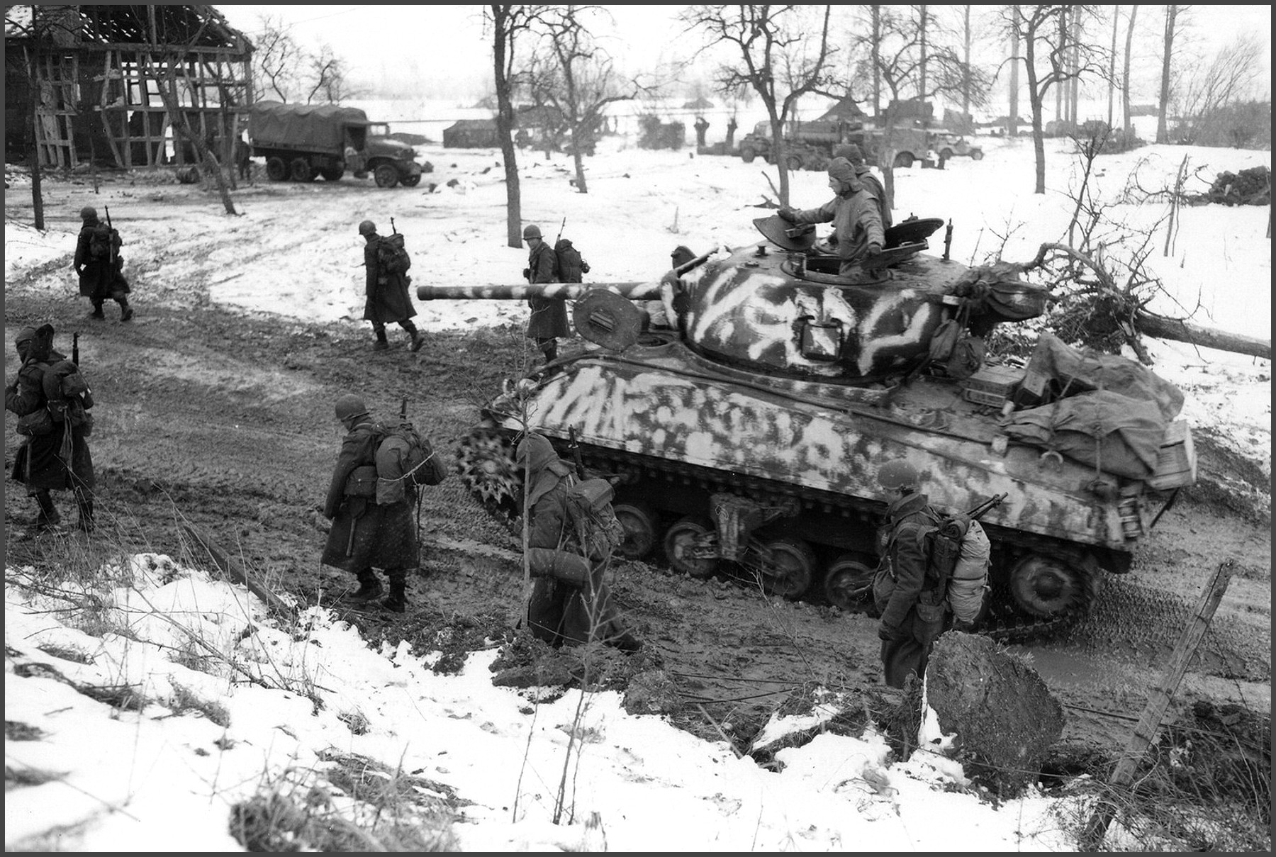 Infantrymen and a camouflaged Sherman Tank of the 12th Armored Division, move through the snow and mud, during the Allied advance on Colmar, France January 1945.